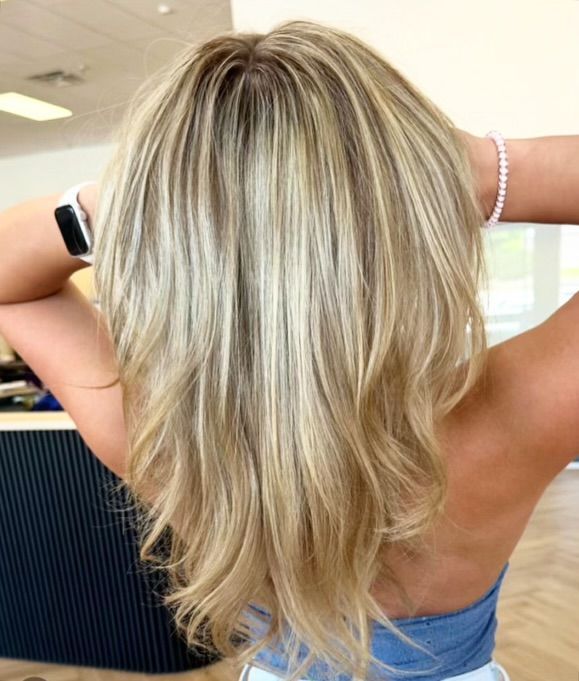 Woman with layered blonde hair, hands up, wearing a light blue top.
