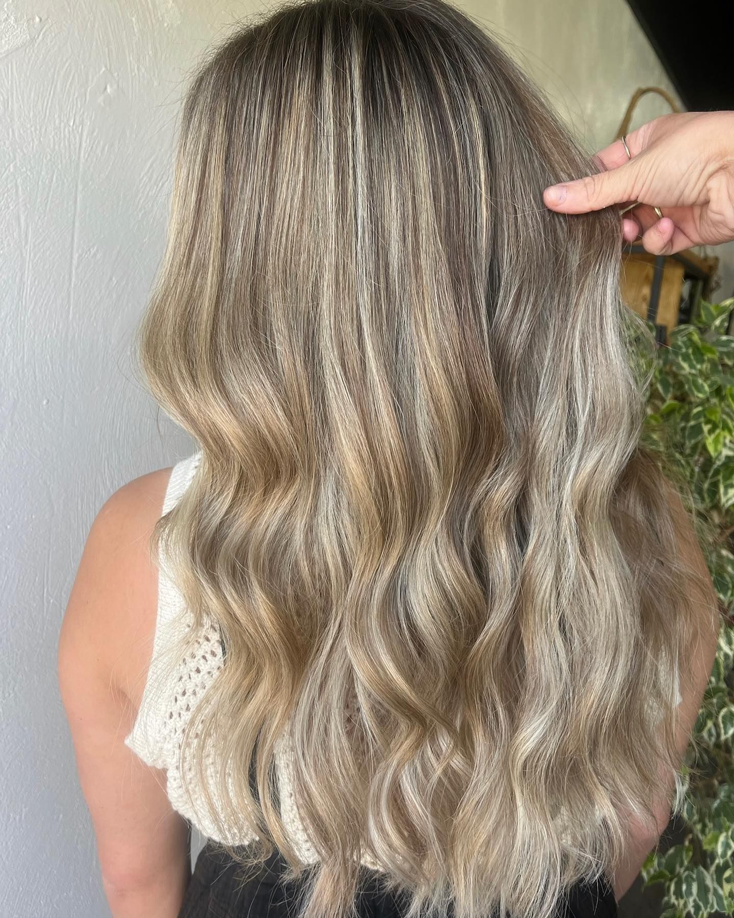 Woman with crimped, ombre blonde hair, wearing a white top. A hand touches the hair.