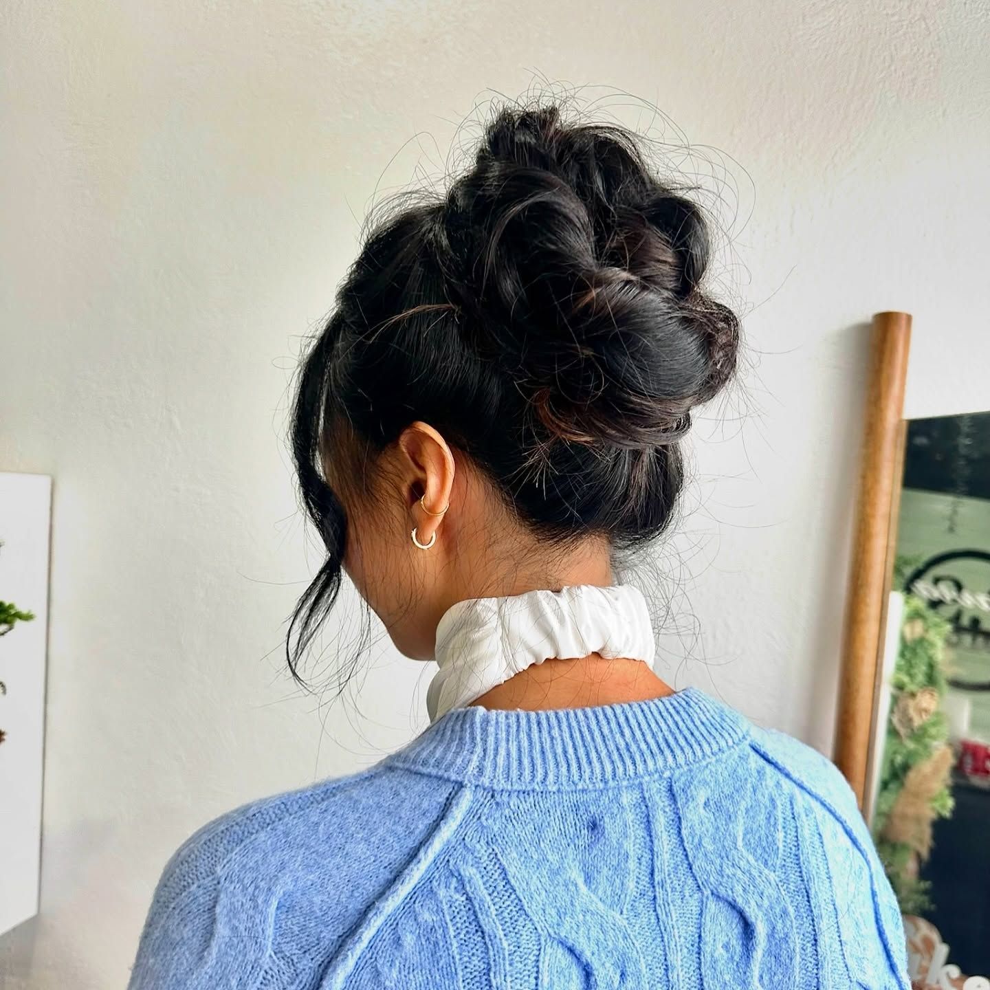 Person with dark hair styled in a high bun, wearing a blue sweater and white ruffled collar.