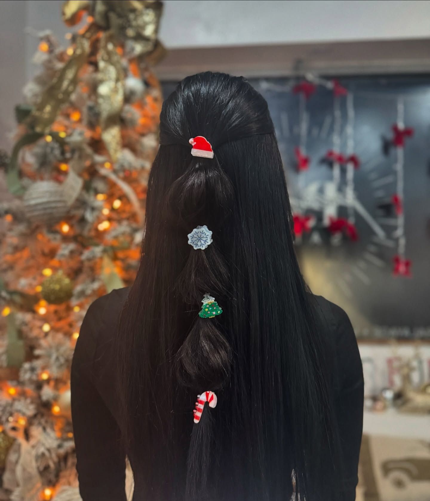 Woman's long, black hair styled with Christmas-themed hair clips in front of a decorated Christmas tree.