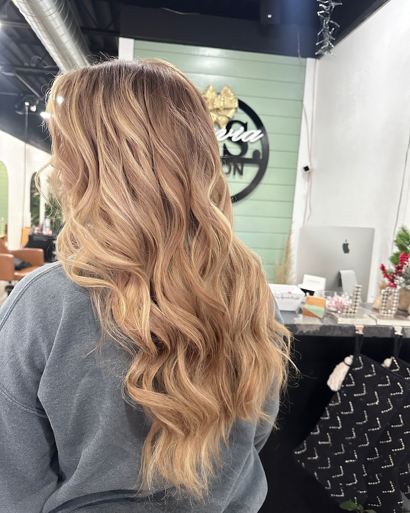 Black-rooted hair transitioning to blonde, seated in a salon chair.