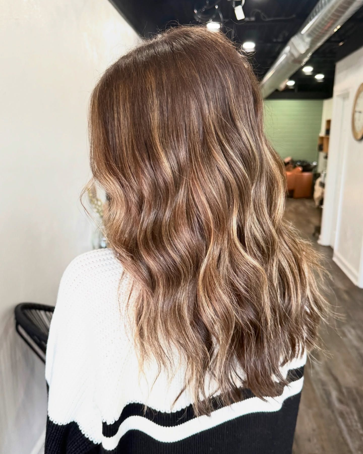 Woman with wavy brown hair, highlights, and a black and white sweater in a salon.