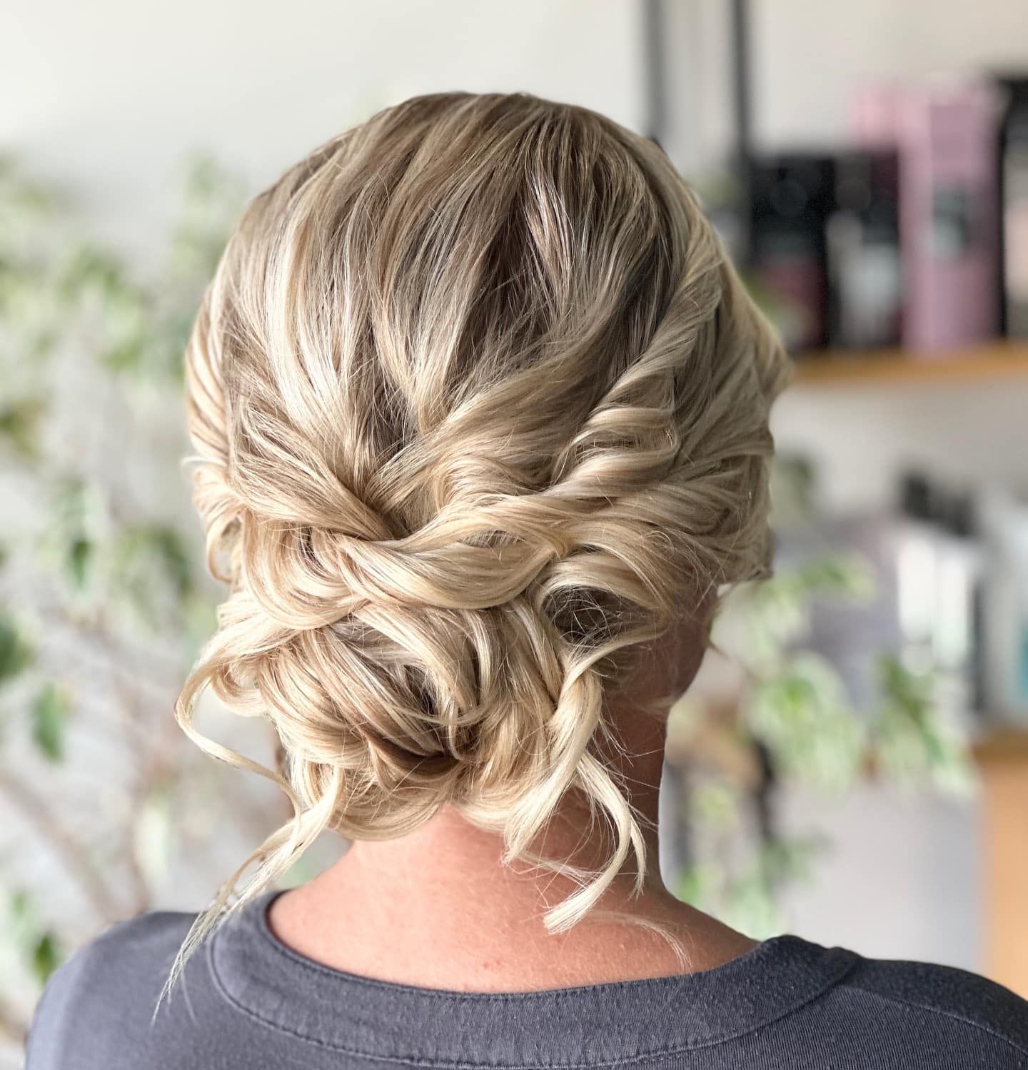 Blonde hair styled in an updo, with curled sections and twists, against a blurred background.