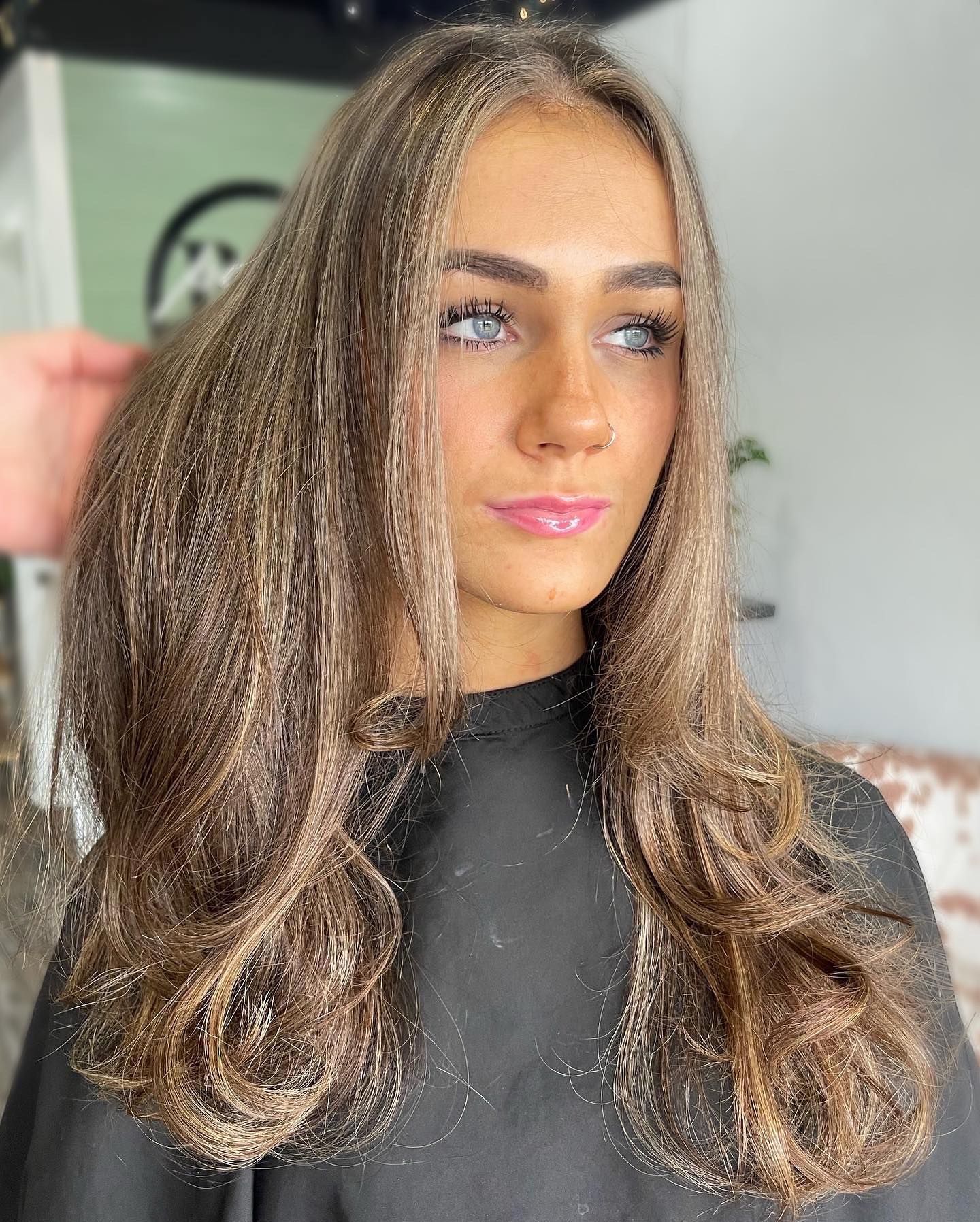 Woman with long, wavy brown hair, styled in a salon, looking toward the side with light blue eyes.