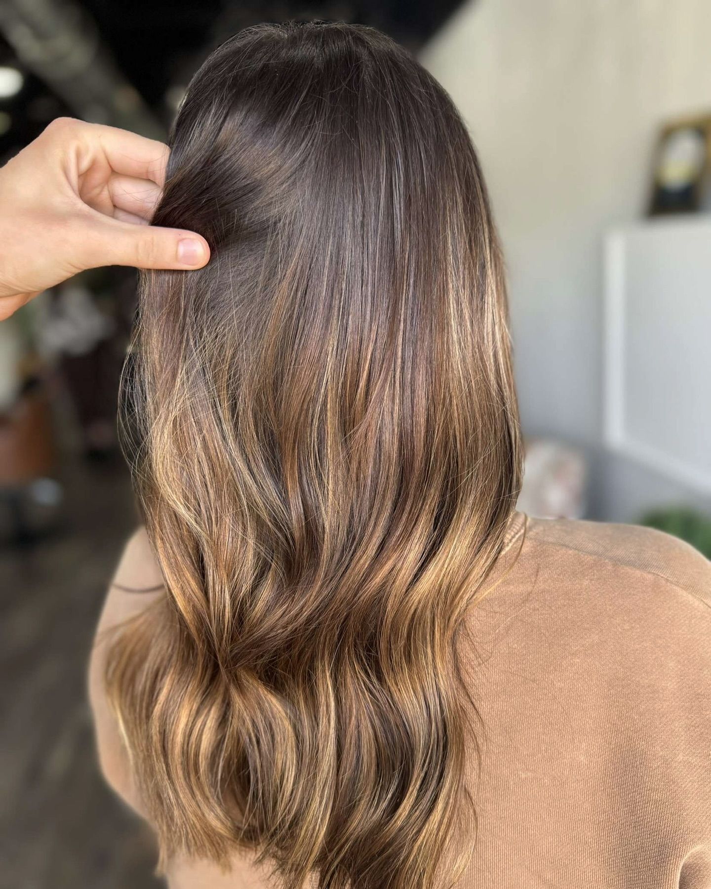 Woman with brown hair, styled with highlights and waves. A hand touches the hair.