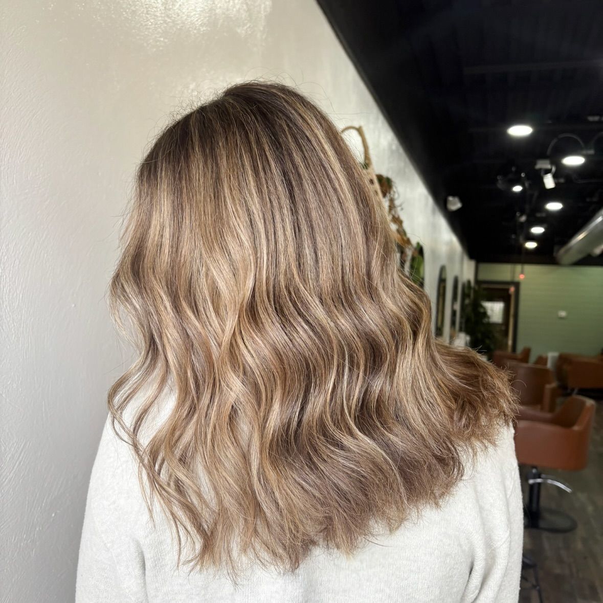 Woman with wavy brown and blonde hair in a salon, wearing a white sweater.