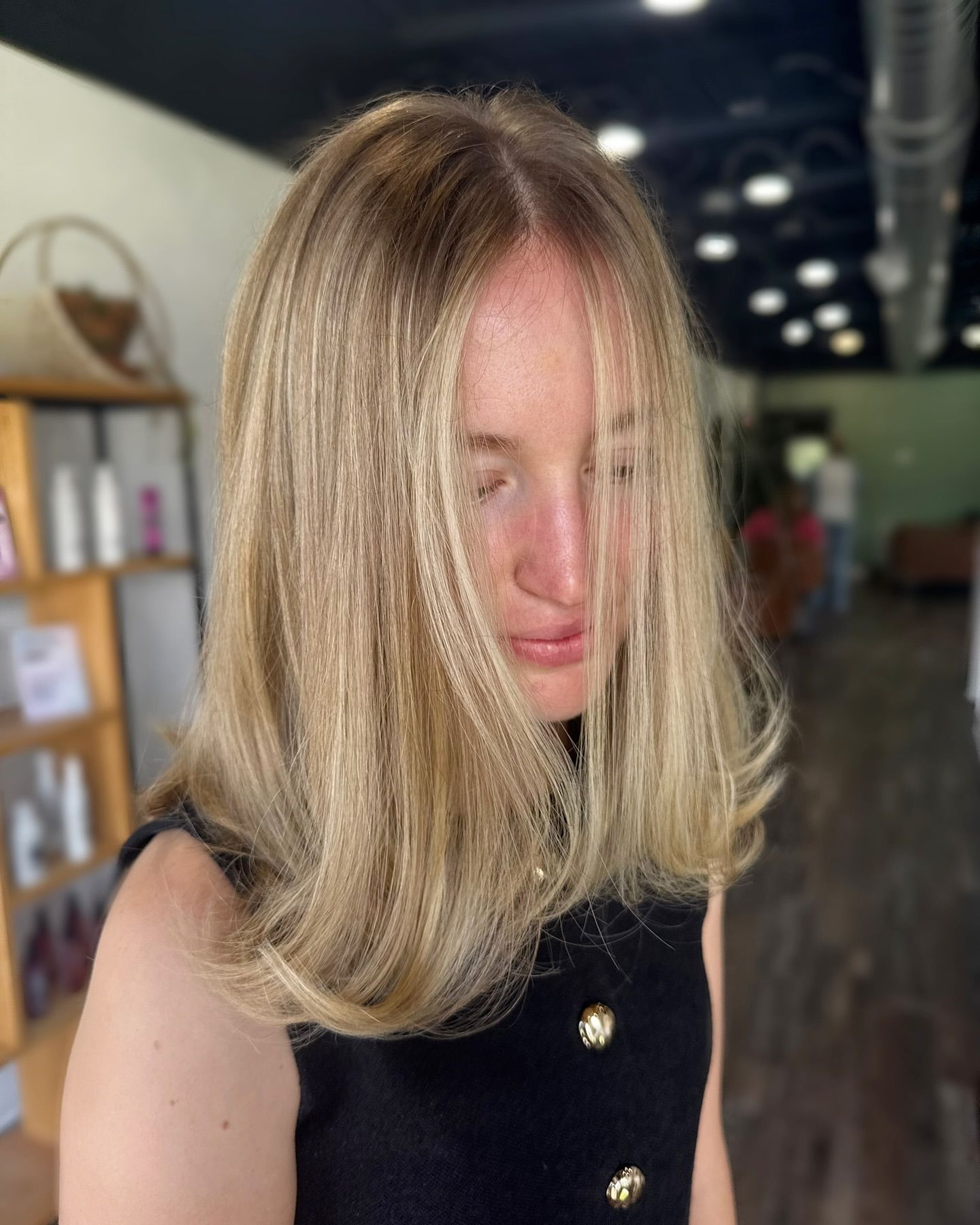 Woman with blonde hair, looking down, in a salon.