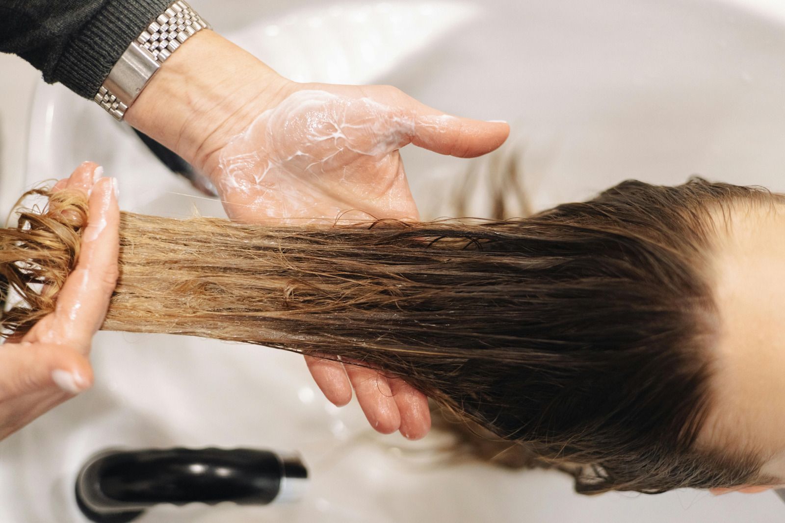 Person's hair being washed with shampoo in a salon sink; hands lathering hair.