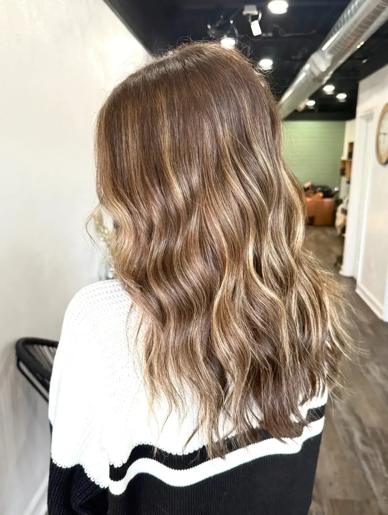 Woman with wavy brown hair and blonde highlights. She wears a black and white sweater.
