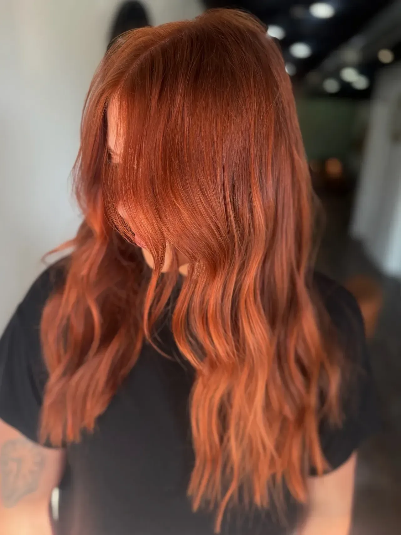 Person with long, wavy auburn hair. Wearing a black top. Hair is down, covering the face.