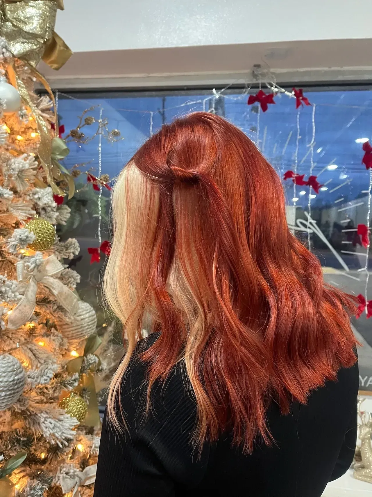 Woman's hair, half reddish-orange, half blonde, styled with waves. Beside a lit Christmas tree.
