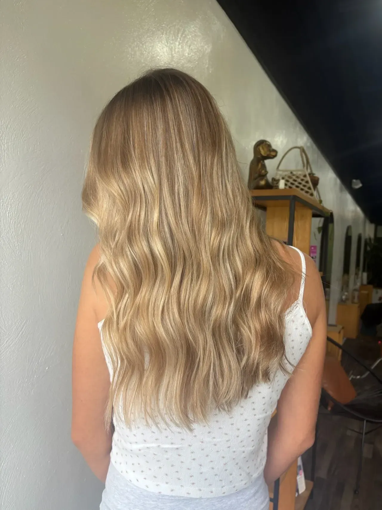 Woman with long, wavy blonde hair in a salon. Wearing a white polka-dot top.