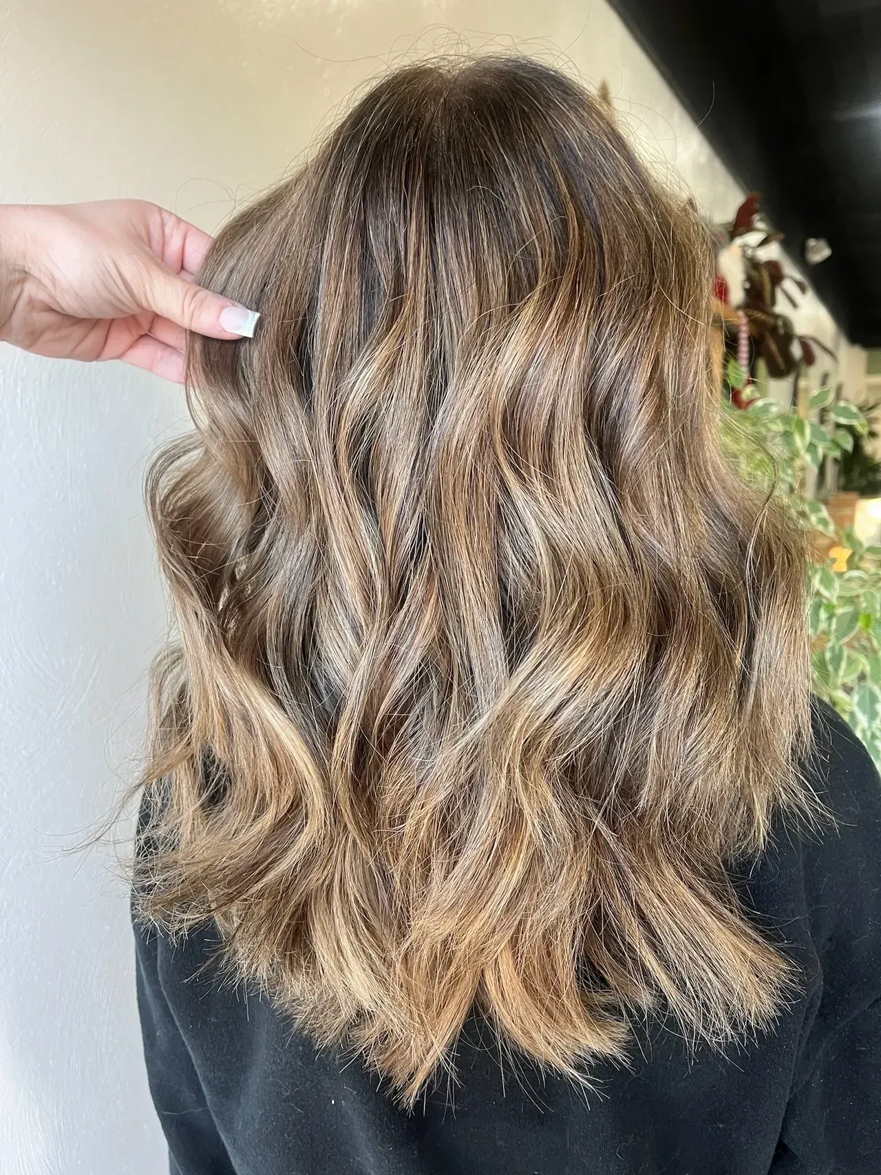 Woman's wavy, brown hair with lighter highlights, being styled, salon setting.