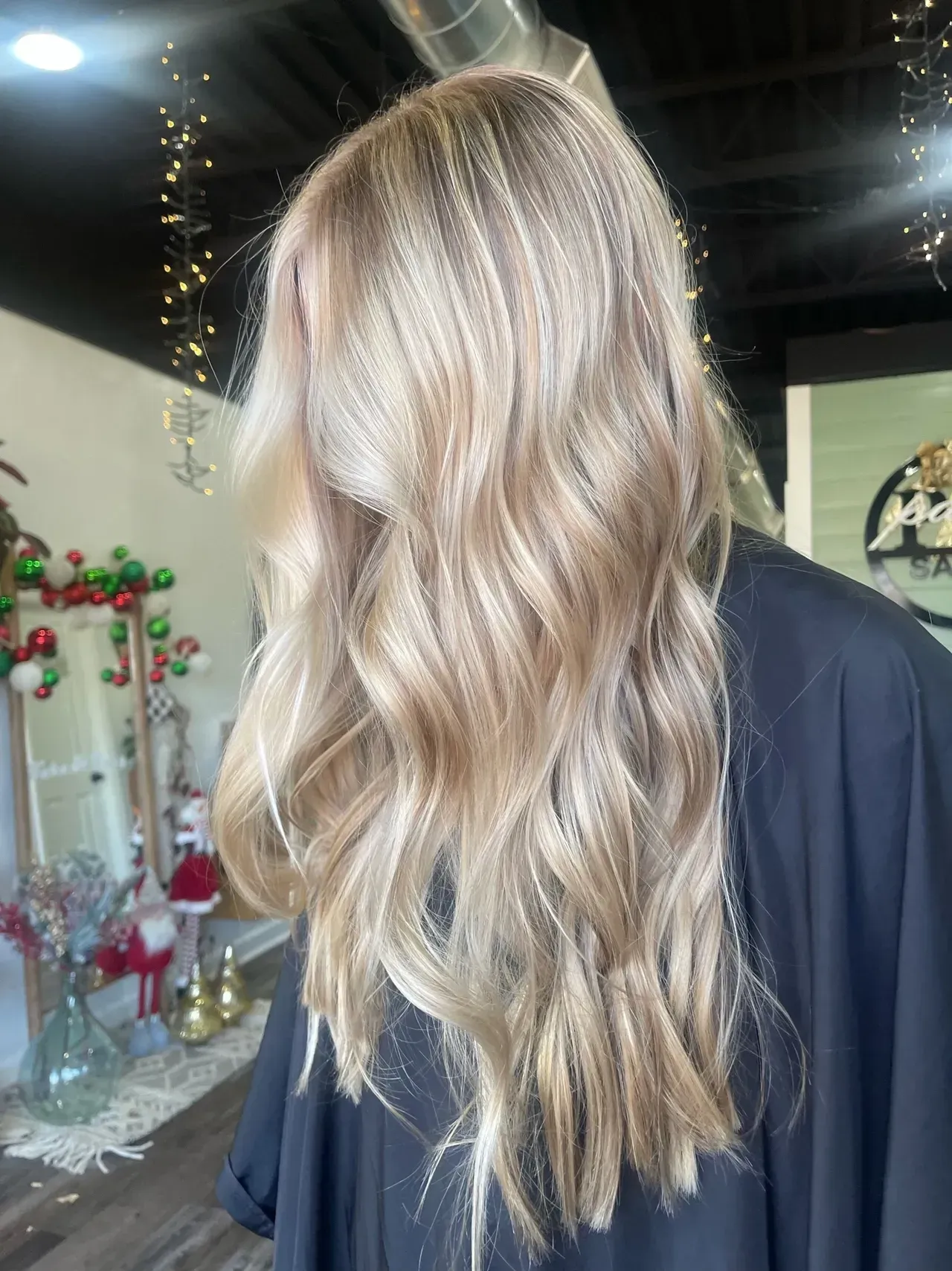 Woman with wavy, light blonde hair in a salon; blurred background with holiday decor.