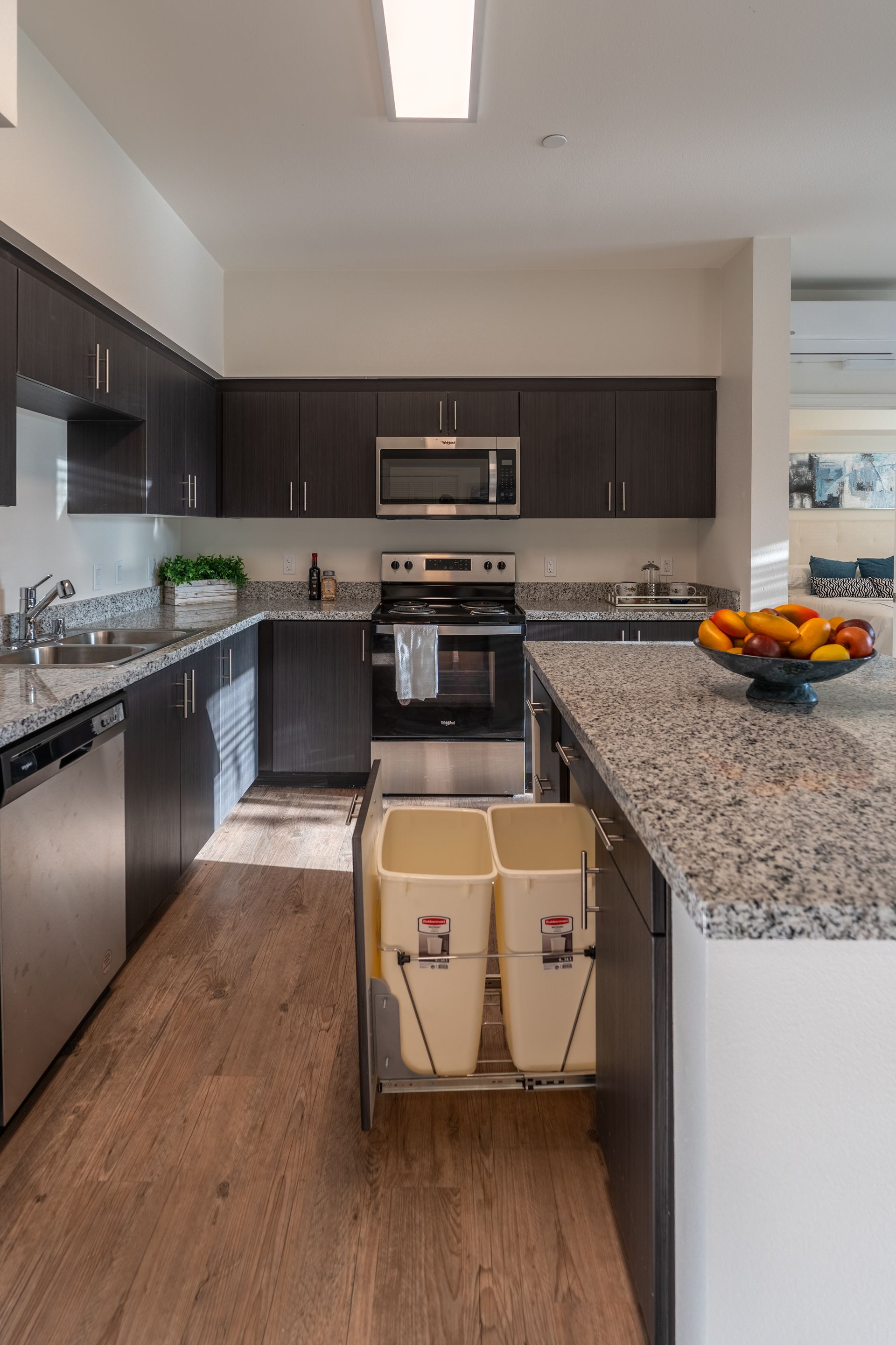 A kitchen with a center island and stainless steel appliances and a drawer pull out trash cans