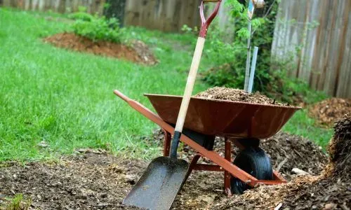 Wheelbarrow and shovel removing bark and soil during a yard tidy, completed in Opoho, Dunedin.