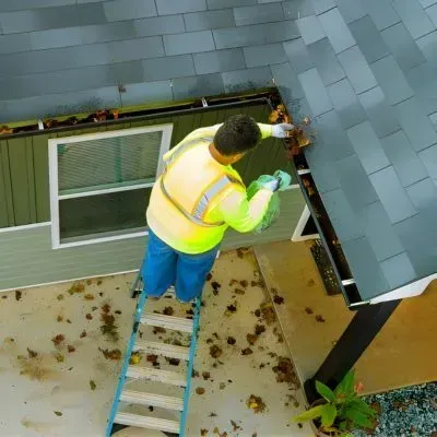 A contractor removing roofline debris from a single-level home, a typical task reflected in gutter-cleaning prices.