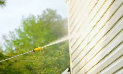 Pressure-washing a house exterior to remove surface buildup during a residential clean in Wakari, Dunedin.