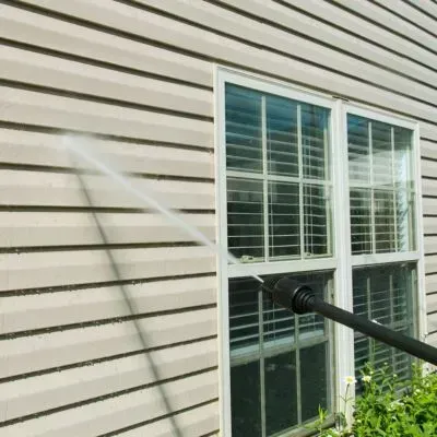 Power washing a house exterior to remove grime and brighten cladding during a clean in Brighton, Dunedin.