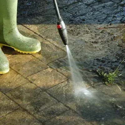 Pressure washing dirty pavers to remove moss and grime and restore proper surface drainage.