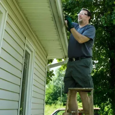 A worker on a short ladder is clearing a gutter on a single-level home in Dunedin, showing safe, low-height access.