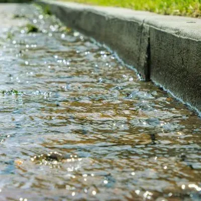 Stormwater runoff flowing along a kerb in Dunedin, showing how contaminants can enter drains without treatment.