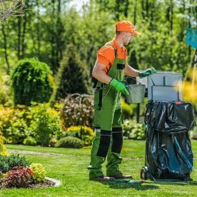 A gardener loading green waste into a bin during a section tidy in Dunedin, showing typical clean-up work.