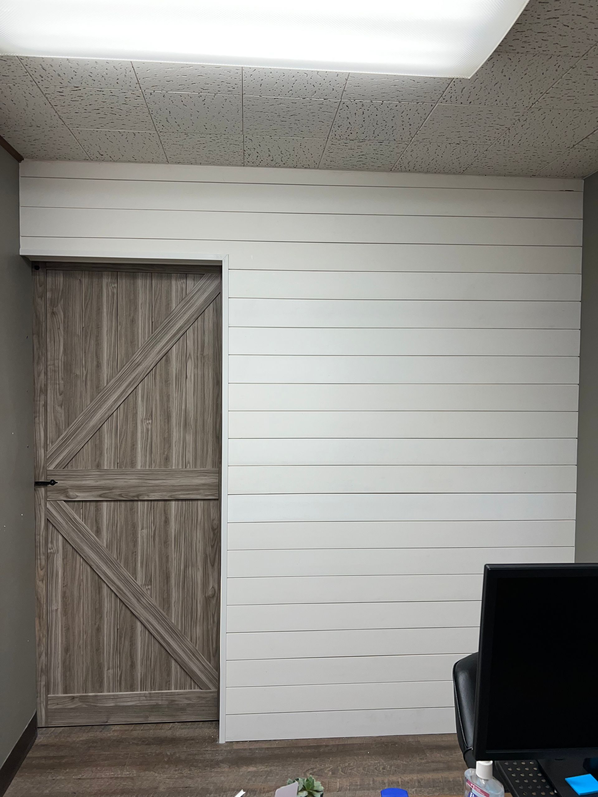 A room with a wooden door and a computer on a desk.