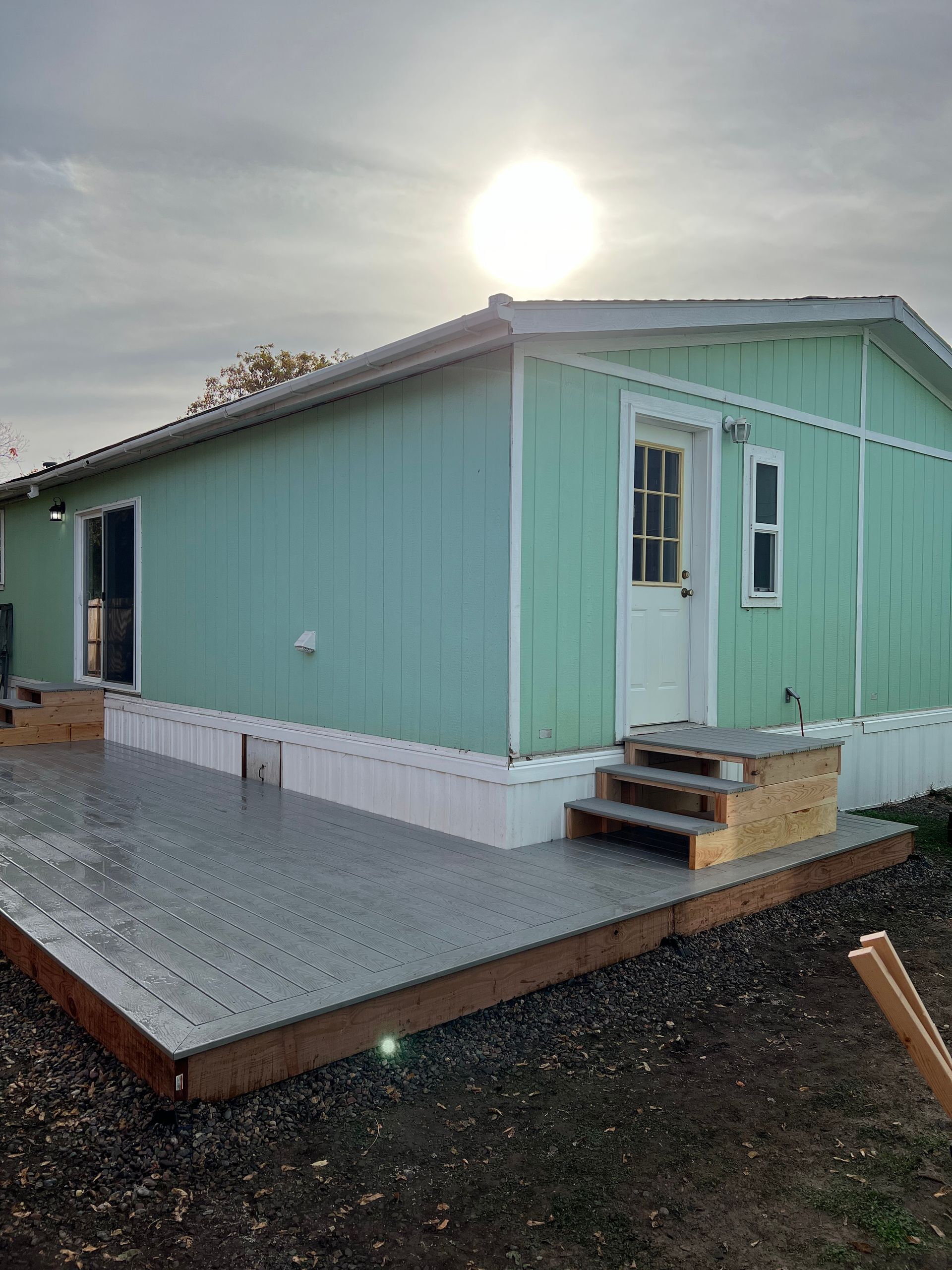A green mobile home with a deck in front of it