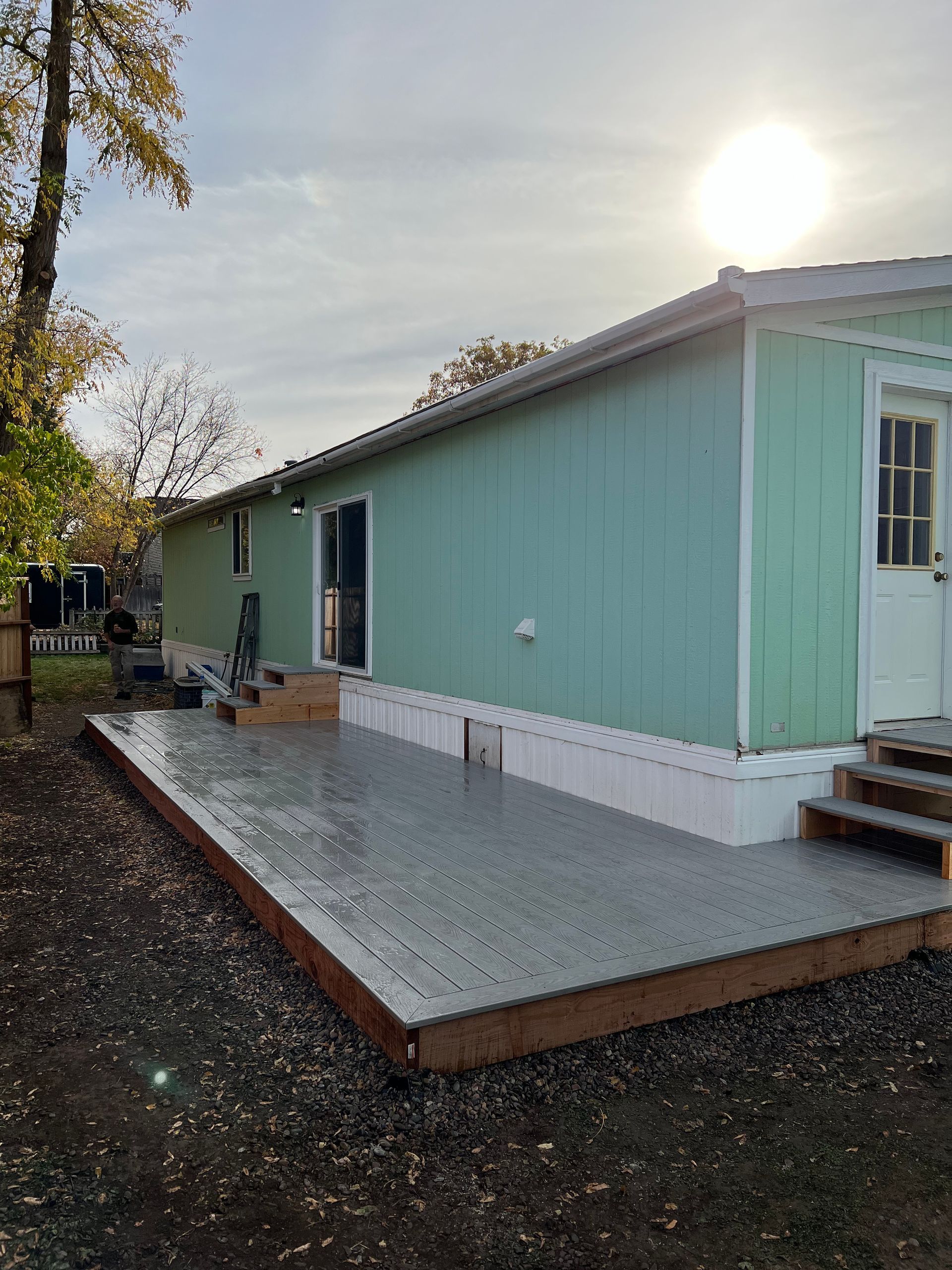 A green mobile home with a deck in front of it
