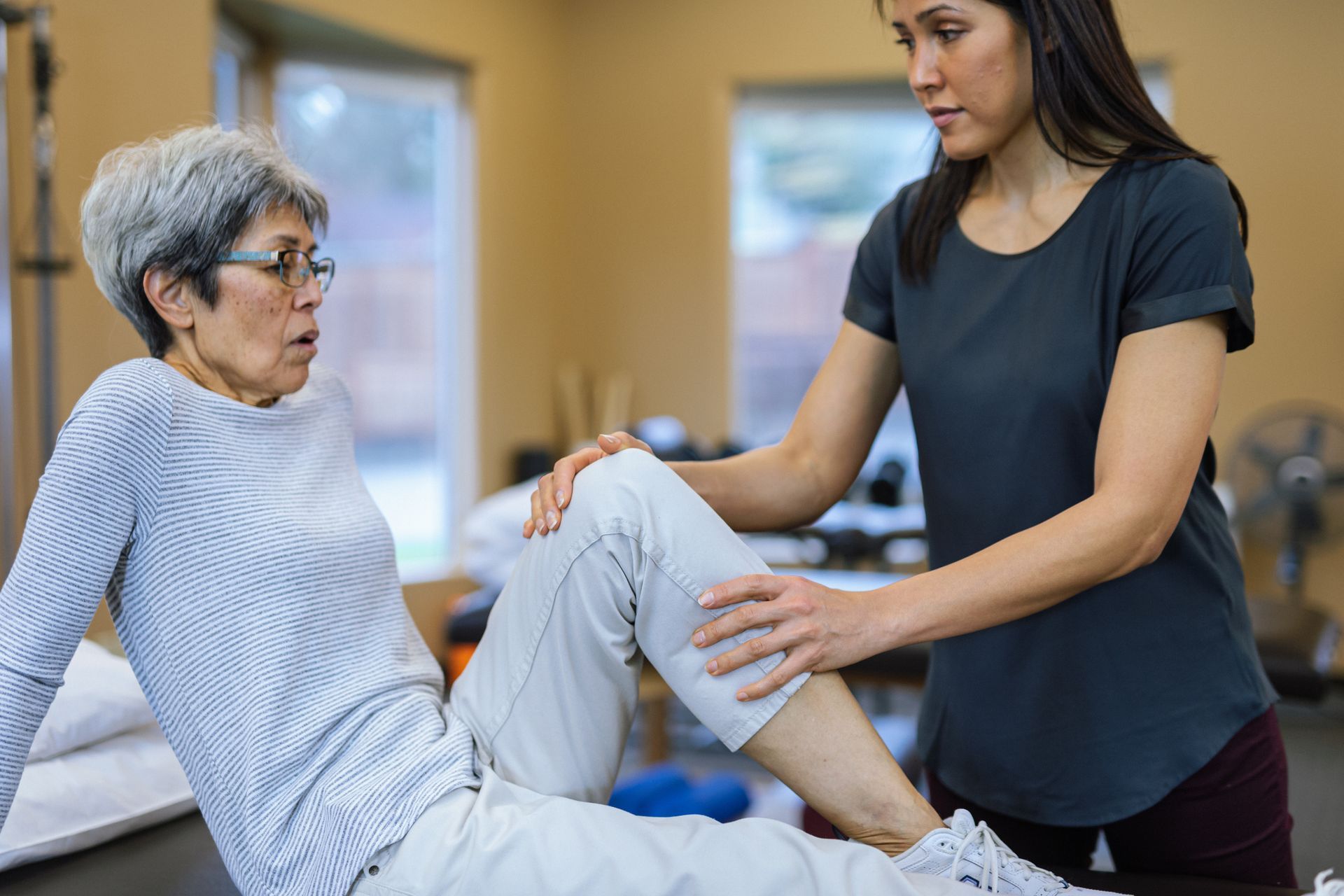 A woman is helping an older woman stretch her leg.