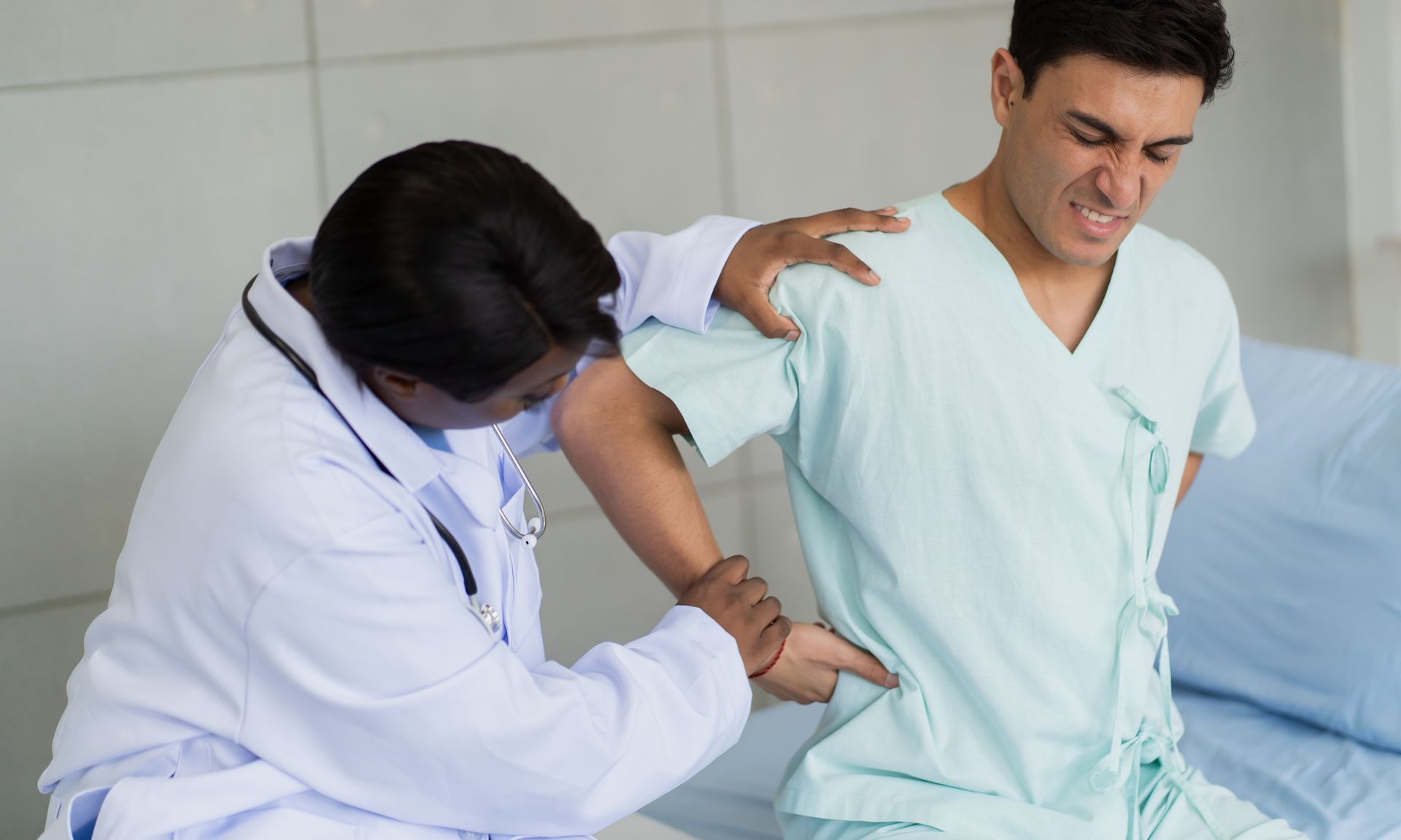 Doctor assisting patient with lower back discomfort during pain management consultation in a clinic Doctor assisting patient with lower back discomfort during pain management consultation in a clinic