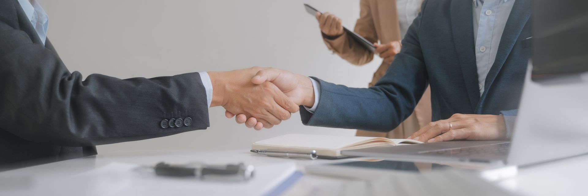 Two professionals shaking hands across a wood desk during a business meeting Two professionals shaking hands across a wood desk during a business meeting