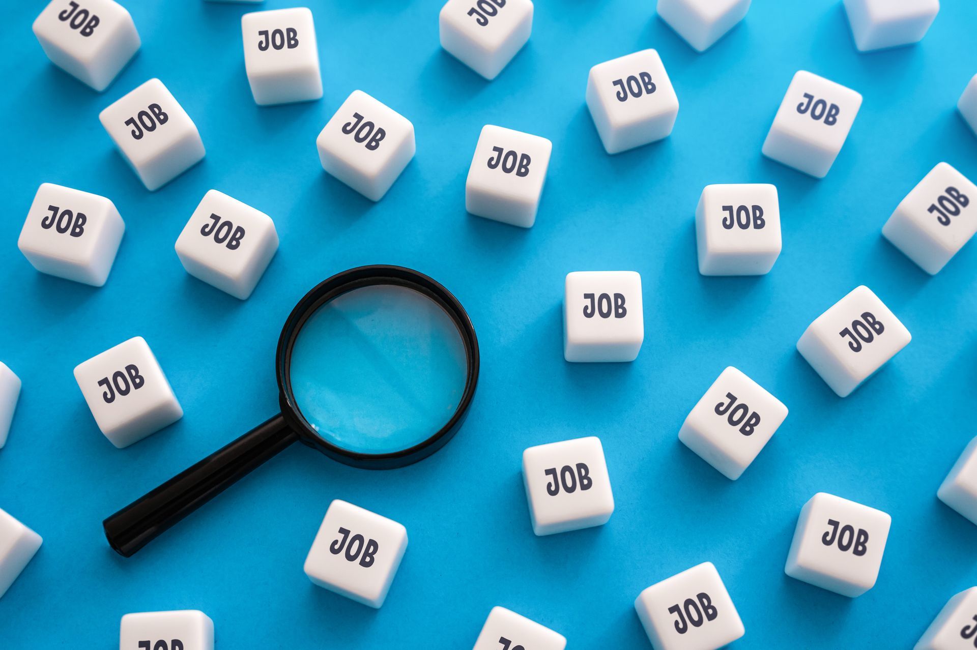 Magnifying glass surrounded by cubes labeled “JOB” on a blue background. Magnifying glass surrounded by cubes labeled “JOB” on a blue background.