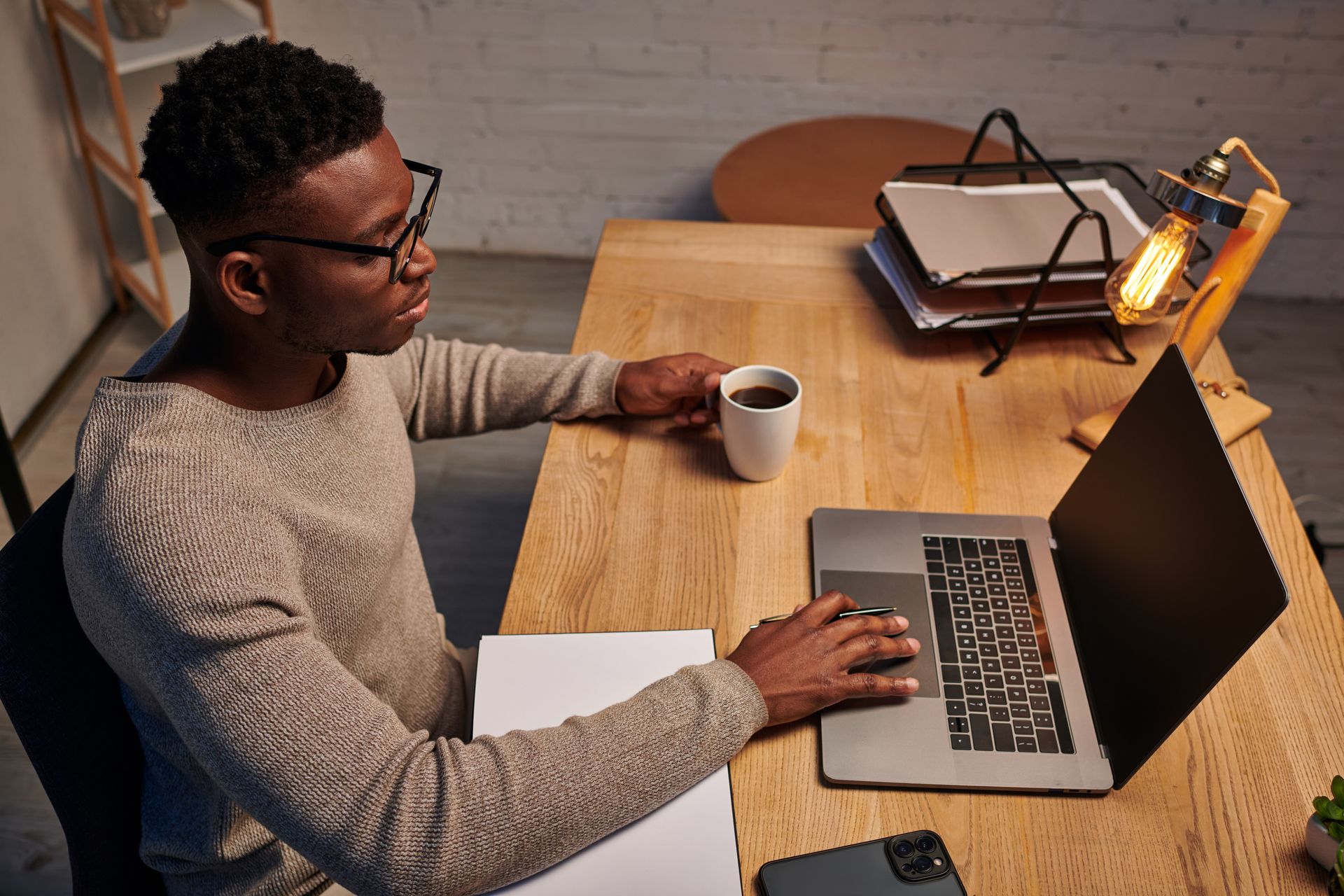 Person working at a wooden desk with laptop, notebook, and cup of coffee.