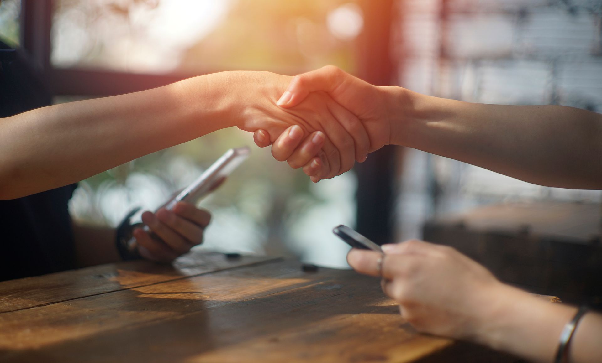 Two people are shaking hands while holding cell phones.