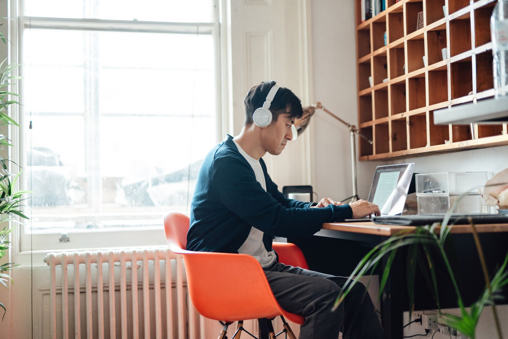 A man wearing headphones is sitting at a desk using a laptop computer.