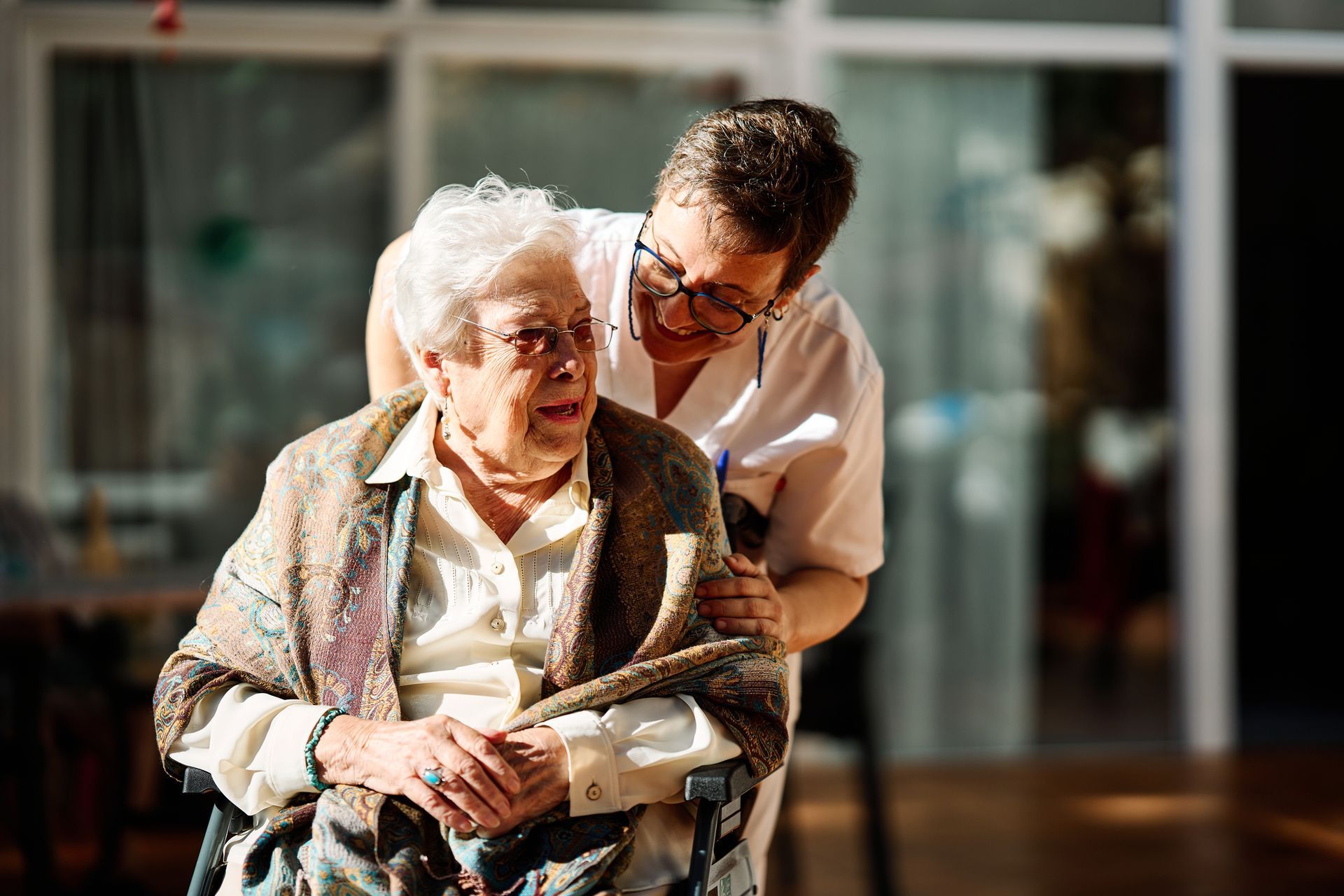 An elderly woman in a wheelchair is being helped by a nurse.