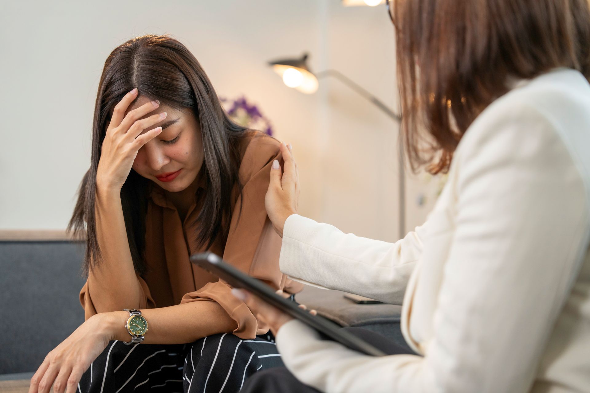 Woman with hand on forehead being consoled by another, indoor setting.