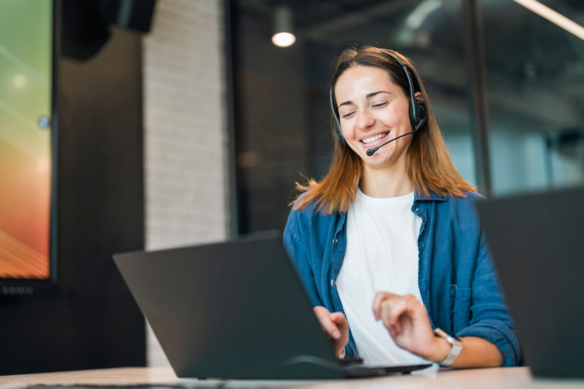 A woman wearing a headset is sitting in front of a laptop computer.