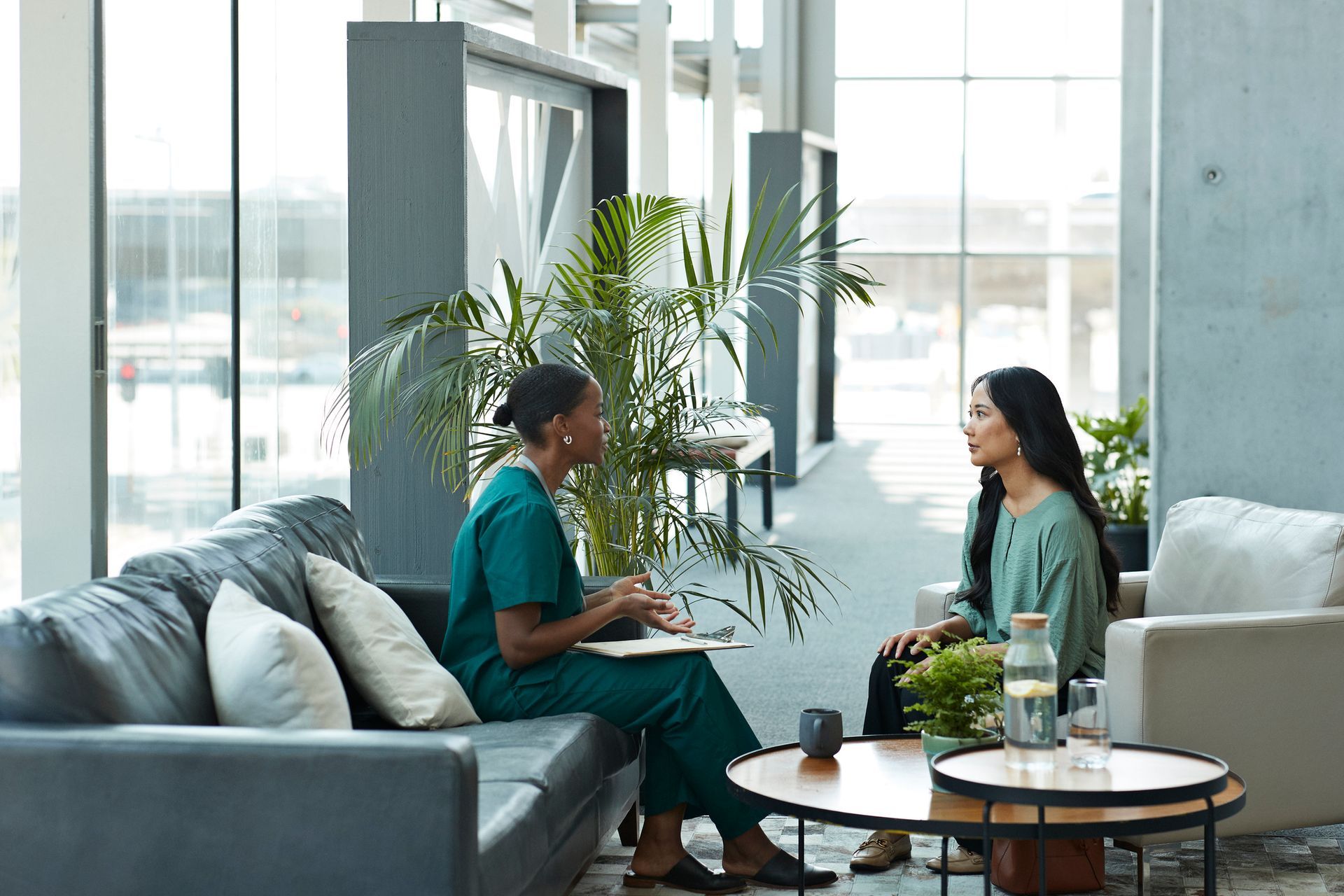 A nurse is sitting on a couch talking to a patient.