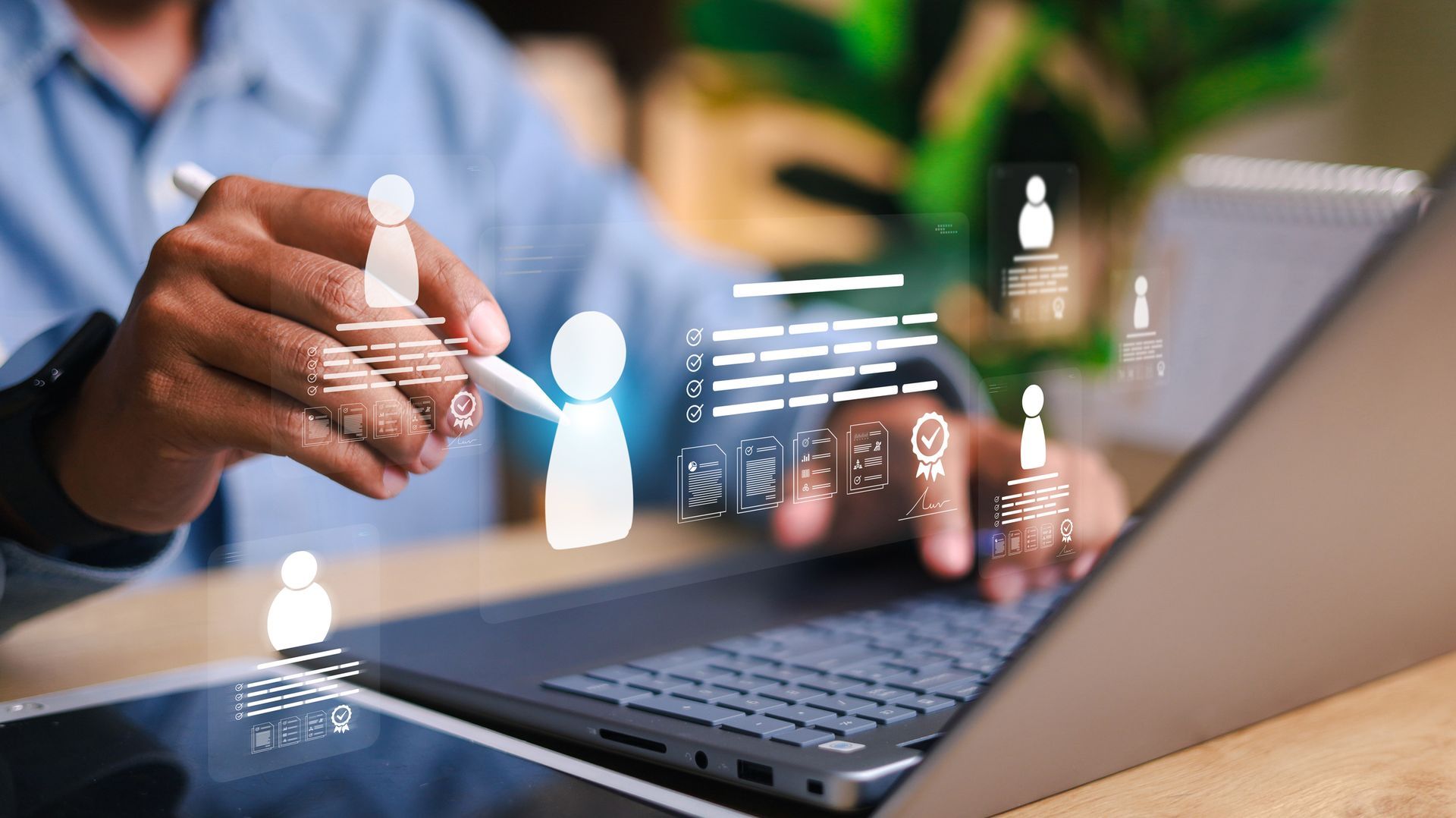 Person using stylus on laptop with holographic data and people icons.