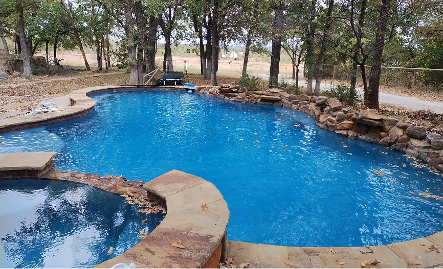 Blue swimming pool with a rock waterfall and surrounding trees.
