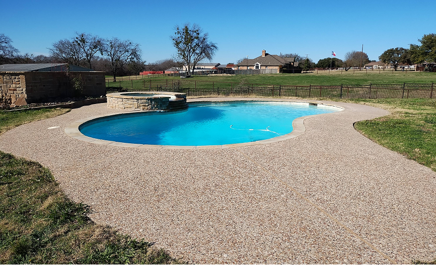 A kidney-shaped swimming pool filled with blue water, surrounded by gravel, in a grassy field.