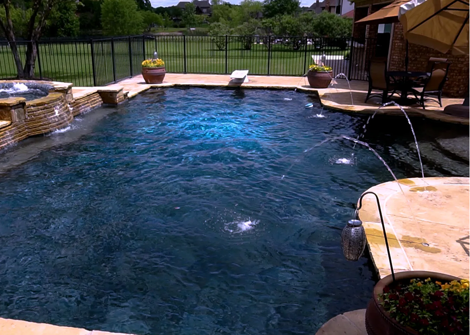 Outdoor pool with dark water, fountains, diving board, and surrounding patio.