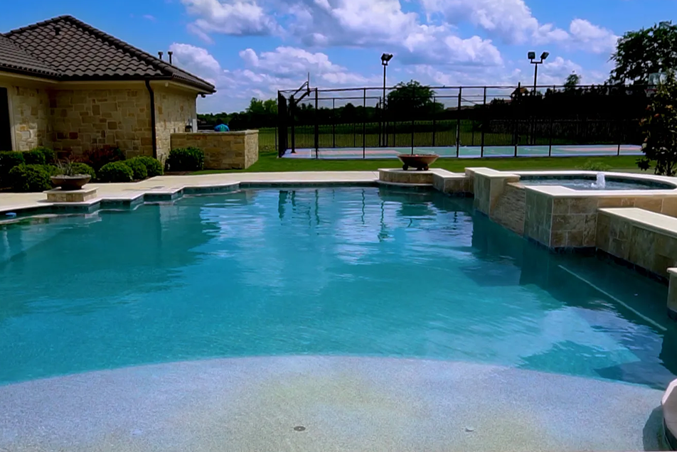 Swimming pool with turquoise water, stone trim, and a tennis court in the background.