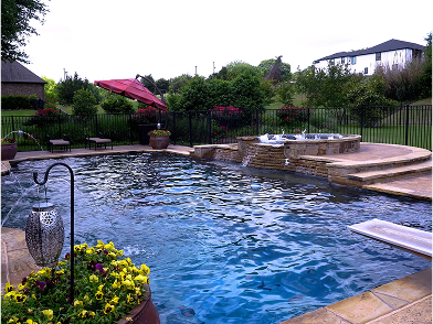 Fire pit with brown glass rocks, next to a pool with a blue surface.