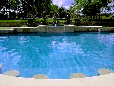 Fire pit with brown glass rocks, next to a pool with a blue surface.