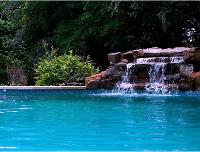 Fire pit with brown glass rocks, next to a pool with a blue surface.