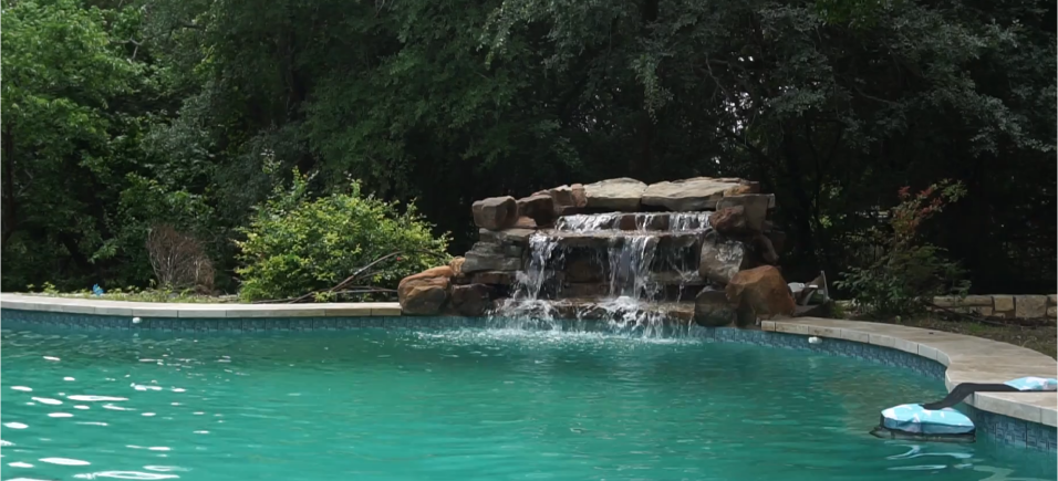 Pool with waterfall surrounded by trees. Turquoise water, brown rocks.